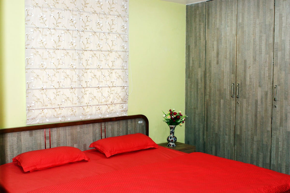 Un dormitorio con cama, mesita de noche, un jarrón con flores y armario.