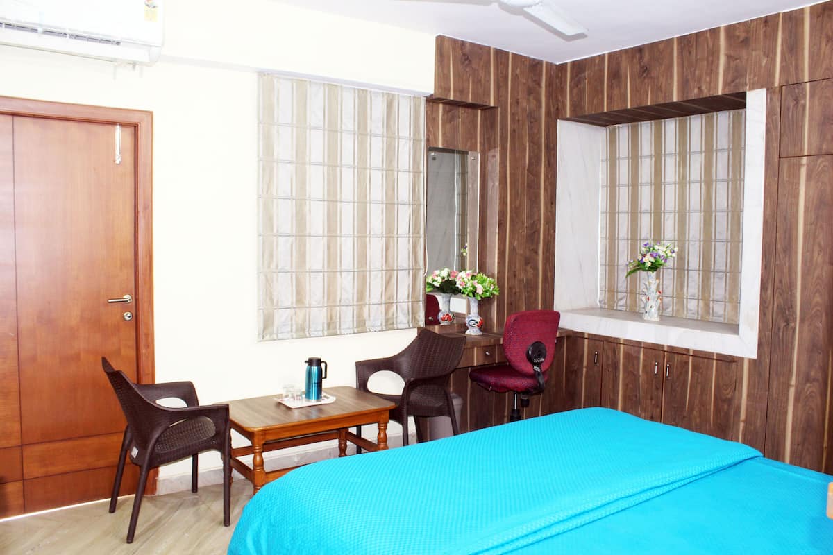 Un dormitorio con cama, escritorio, dos sillas, espejo y ventana con vistas.