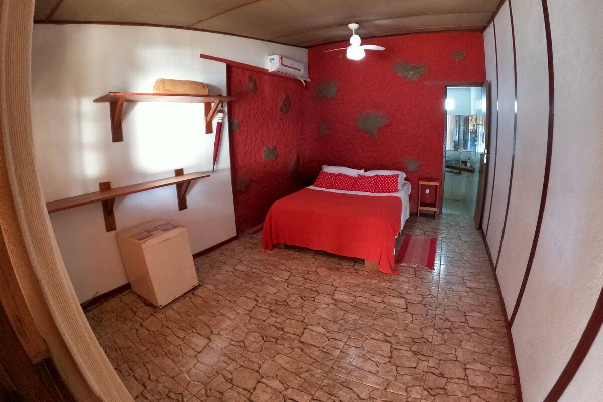 Ein Schlafzimmer mit einem Bett, einem kleinen Tisch, einem Regal, einem Kleiderschrank und einem Deckenventilator.