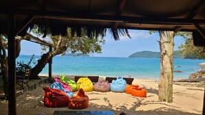 A beachside seating area with colorful bean bags and a table under a thatched roof, overlooking the sea. - Cabanas Paraiso (Angra dos Reis)