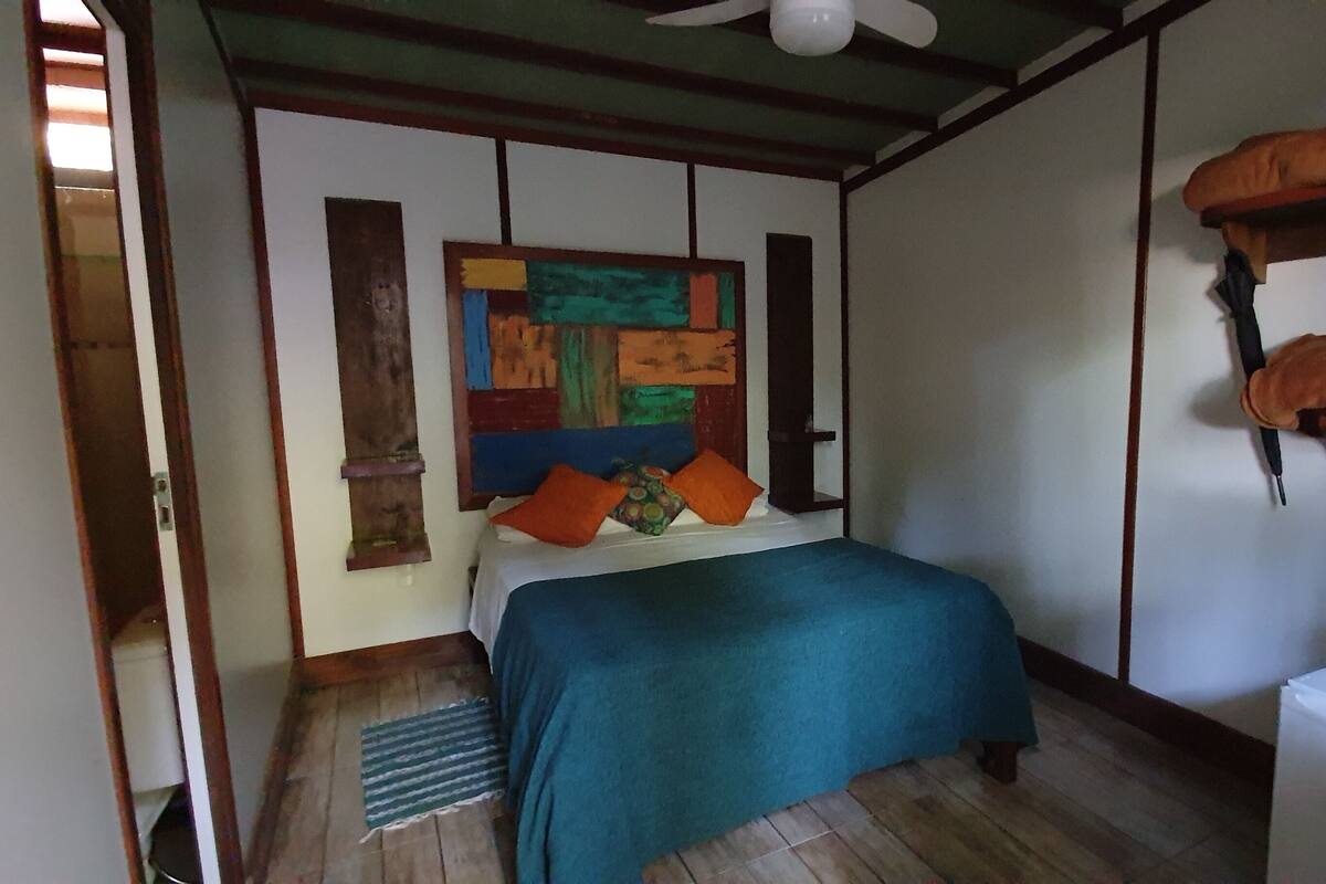 Ein Schlafzimmer mit einem Bett, einem farbenfrohen abstrakten Gemälde an der Wand und einem kleinen weißen Gerät rechts.