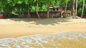 A beach with wooden structures, some with thatched roofs, and a sandy beach with gentle waves. - Cabanas Paraiso (Angra dos Reis)