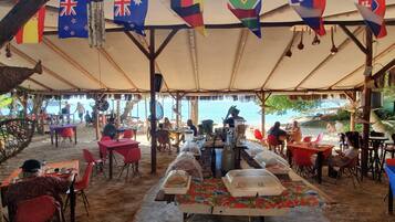 An outdoor dining area with tables and chairs, flags hanging above, and a view of the sea.