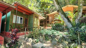 A rustic building with a green exterior and a red section, surrounded by lush vegetation and rocks. - Cabanas Paraiso (Angra dos Reis)