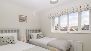 Un dormitorio con dos camas, una ventana que da a vistas de casas, un cuadro en la pared y un radiador.