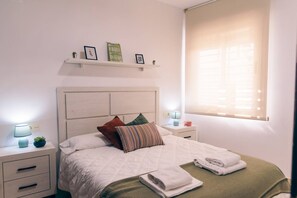 Un dormitorio con cama, mesitas de noche, una ventana con persianas y adornos en la pared.