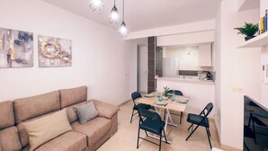 Ein modernes Wohnzimmer mit einem beigen Sofa, einem Esstisch mit Stühlen und einer durchgehenden Tür erkennbaren Küche.