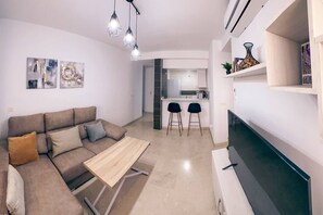 A modern living room with a sofa, coffee table, and TV. There is a kitchen area with a dining set and a refrigerator. - Yaye House, Écija (Ecija)