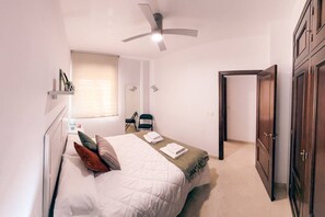 A bedroom with a bed, a ceiling fan, a window, a chair, and a wardrobe.