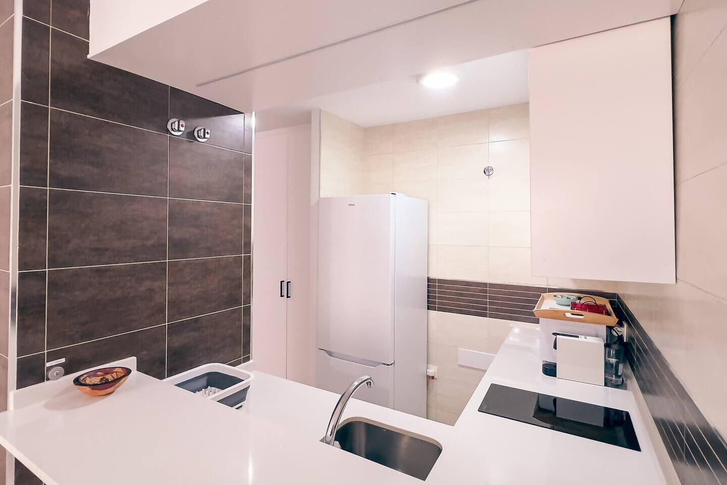 A modern kitchen with a white countertop, a built-in sink, and a refrigerator.