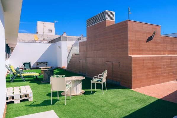 A rooftop terrace with a green lawn, a round table, and two chairs.