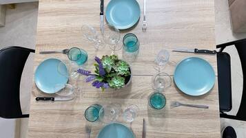 Una mesa de comedor dispuesta con platos azules, cubiertos y vasos, rodeada de sillas.