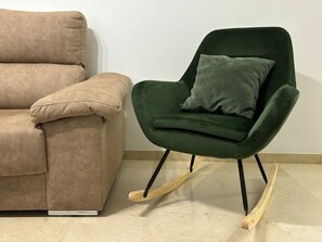 Un sofá color beige y un sillón mecedora verde con cojín.