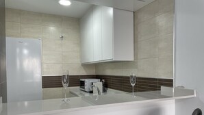 Eine moderne Küche mit weißen Schränken, einem Kühlschrank, einer Mikrowelle und zwei Weingläsern auf der Arbeitsfläche.