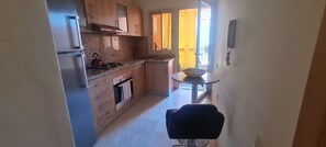 Uma cozinha compacta com armários de madeira, fogão a gás e uma pequena área de refeições com mesa e cadeira.