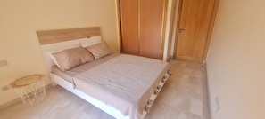 Quarto com cama, guarda-roupa de madeira e um banquinho redondo de vime.