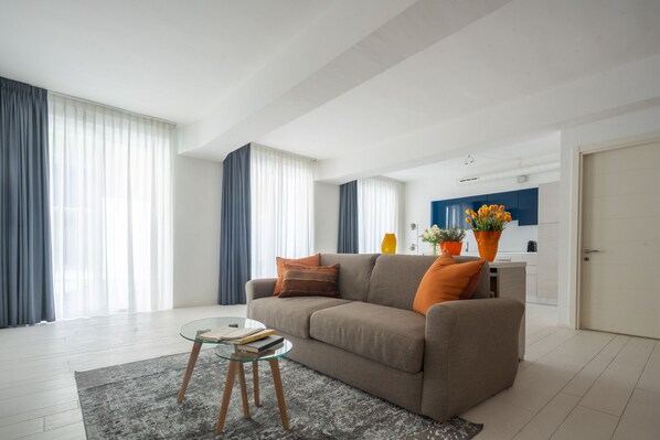 A modern living room with a sofa, a glass coffee table, and a kitchen in the background. - App 6 - Centrale Mazzoni (Venecia)