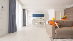 A modern living room with a sofa, a dining table, and a kitchen in the background. - App 6 - Centrale Mazzoni (Venecia)