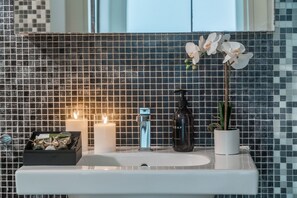 A bathroom with a tiled backsplash, a white sink, a mirror, two lit candles, a soap dispenser, and a potted plant. - App 6 - Centrale Mazzoni (Venecia)