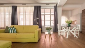 Ein modernes Wohnzimmer mit einem gelben Sofa, einem runden Glastisch und weißen Stühlen sowie einer Blumentopf-Pflanze.