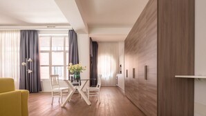 Ein modernes Wohnzimmer mit Esstisch, zwei Stühlen, einem gelben Sessel und einem großen Fenster mit Vorhängen.