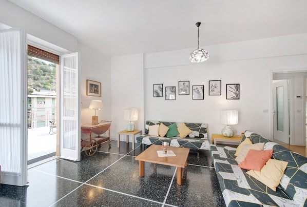 Un salon moderne avec un canapé, une table basse et des lampes. Une porte donne sur l’extérieur, et des œuvres d’art ornent le mur.