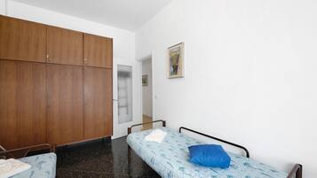 Ein Zimmer mit zwei Einzelbetten, einem Holzschrank, einer Tür zu einem anderen Raum und einem gerahmten Bild an der Wand.