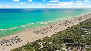 Uma praia com águas turquesa cristalinas, areal arenoso e um conjunto denso de palmeiras.