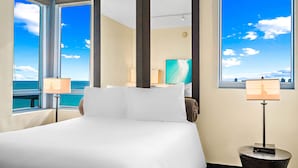 Quarto de hotel com uma cama grande, duas luminárias de cabeceira, uma televisão e vista para o oceano.