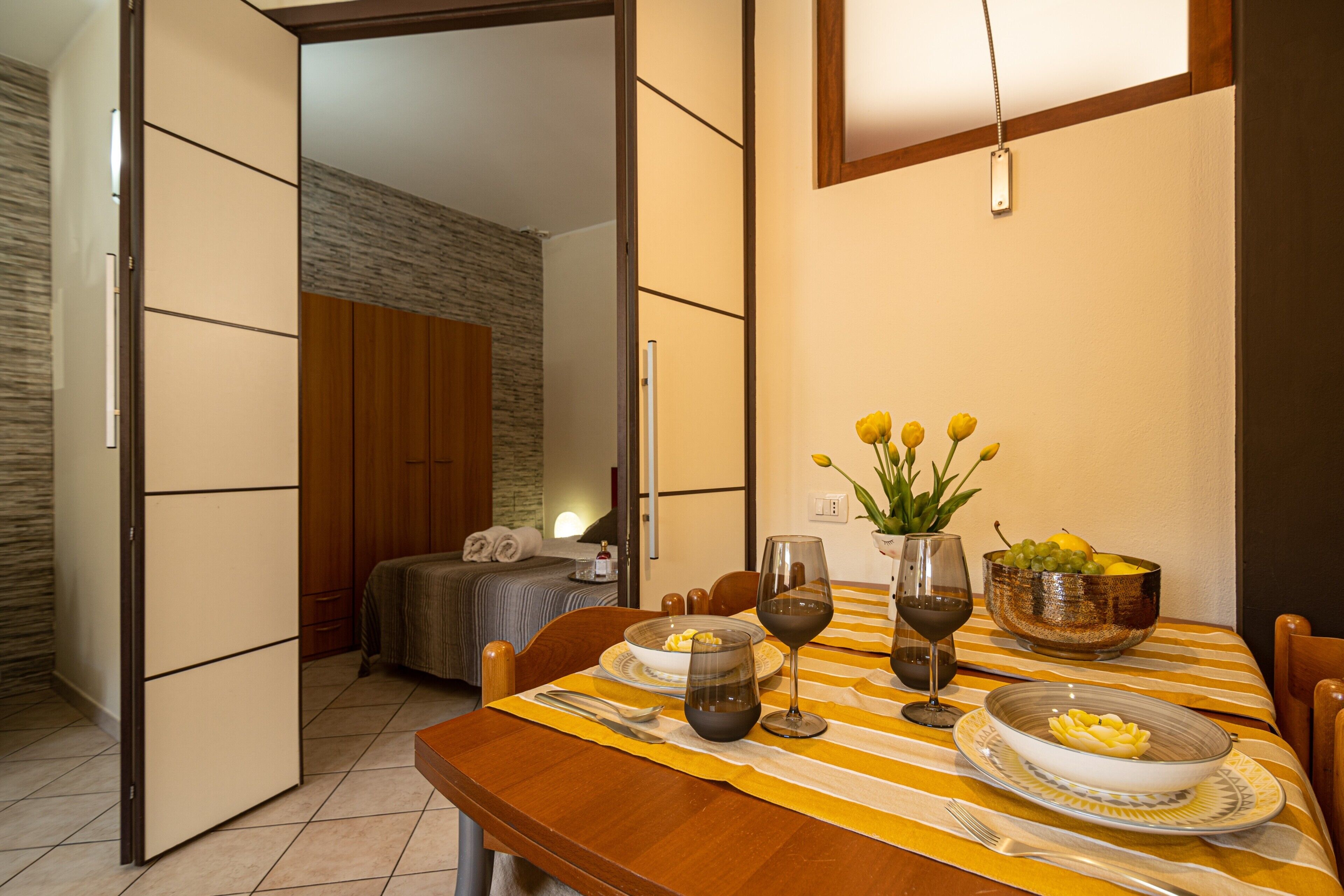 Un coin repas avec une table dressée pour deux personnes, un lit en arrière-plan et une armoire en bois.