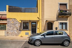 A two-story building with a stone facade, a balcony with a metal railing, and a parked silver car. - Holiday Home Casa Niluca close to the Beach with A/C (Portoscuso)