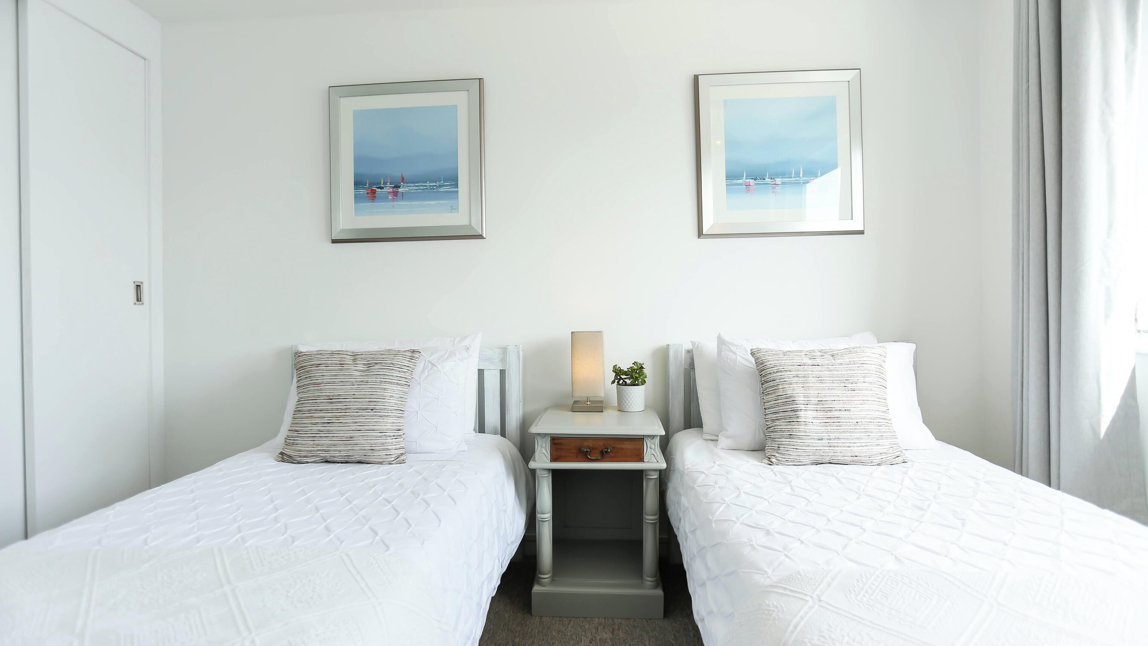 A hotel room with two beds, a nightstand with a lamp, and two framed pictures on the wall.