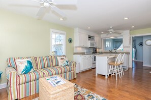 A modern kitchen with white cabinets, a central island, and a dining area with white chairs. - Playin Hooky - Charming 3 Br/2 Ba Cottage!  Linens included for weekly stays! (Topsail Beach)
