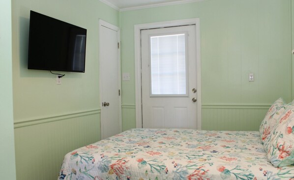 A room with a bed, a television mounted on the wall, and a door with a window.