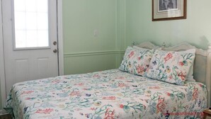 Ein Schlafzimmer mit einem blumigen Bettüberwurf, einer weißen Tür und einem gerahmten Bild an der Wand.