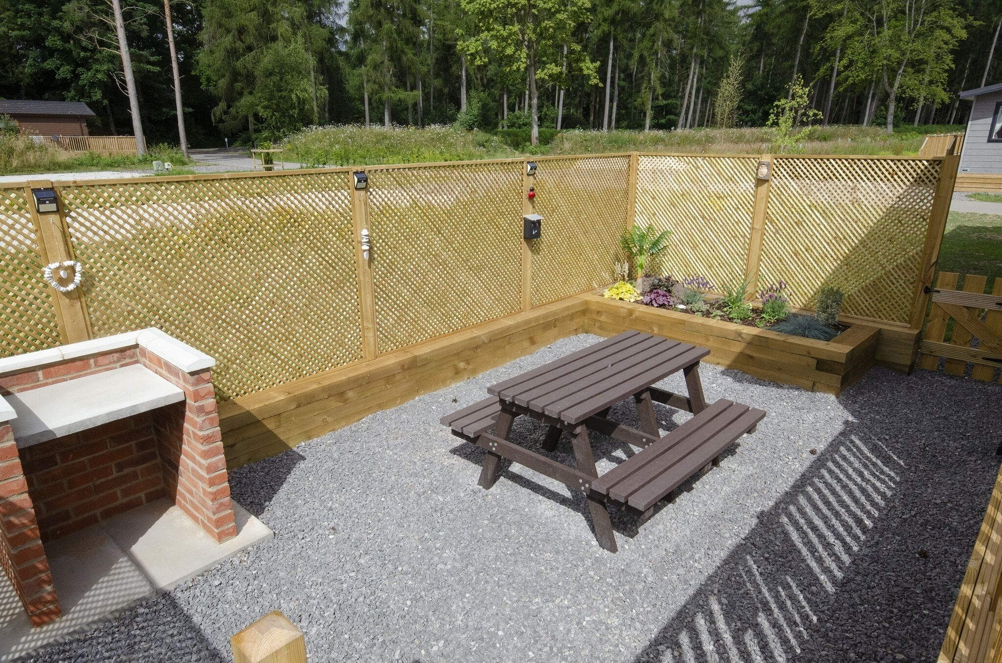 A backyard with a wooden fence, a brick barbecue, and a picnic table.