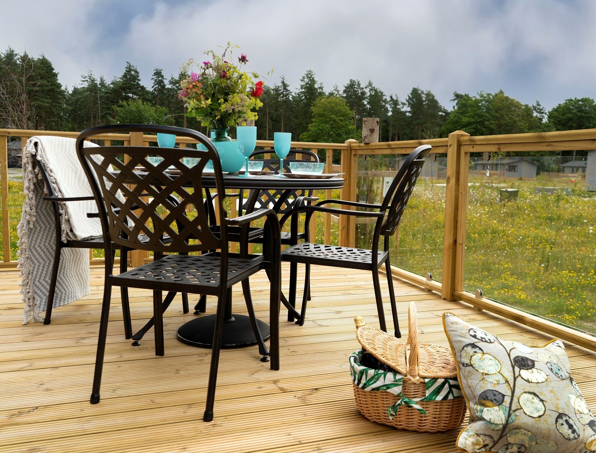 Una terraza de madera con una mesa, sillas, una cesta de mimbre y un cojín.