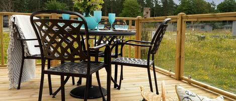 A wooden deck with a table and chairs, a wicker basket, and a cushion.