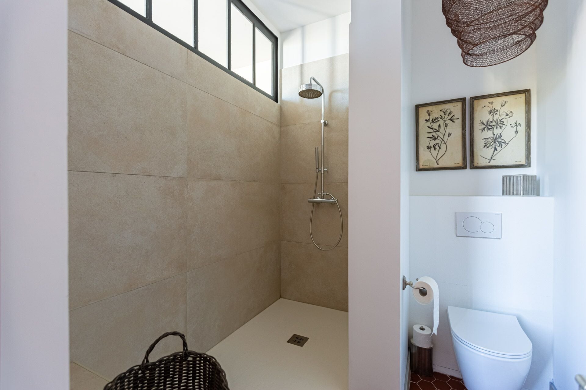 Ein Badezimmer mit Dusche, Toilette und zwei gerahmten Pflanzenbildern an der Wand.