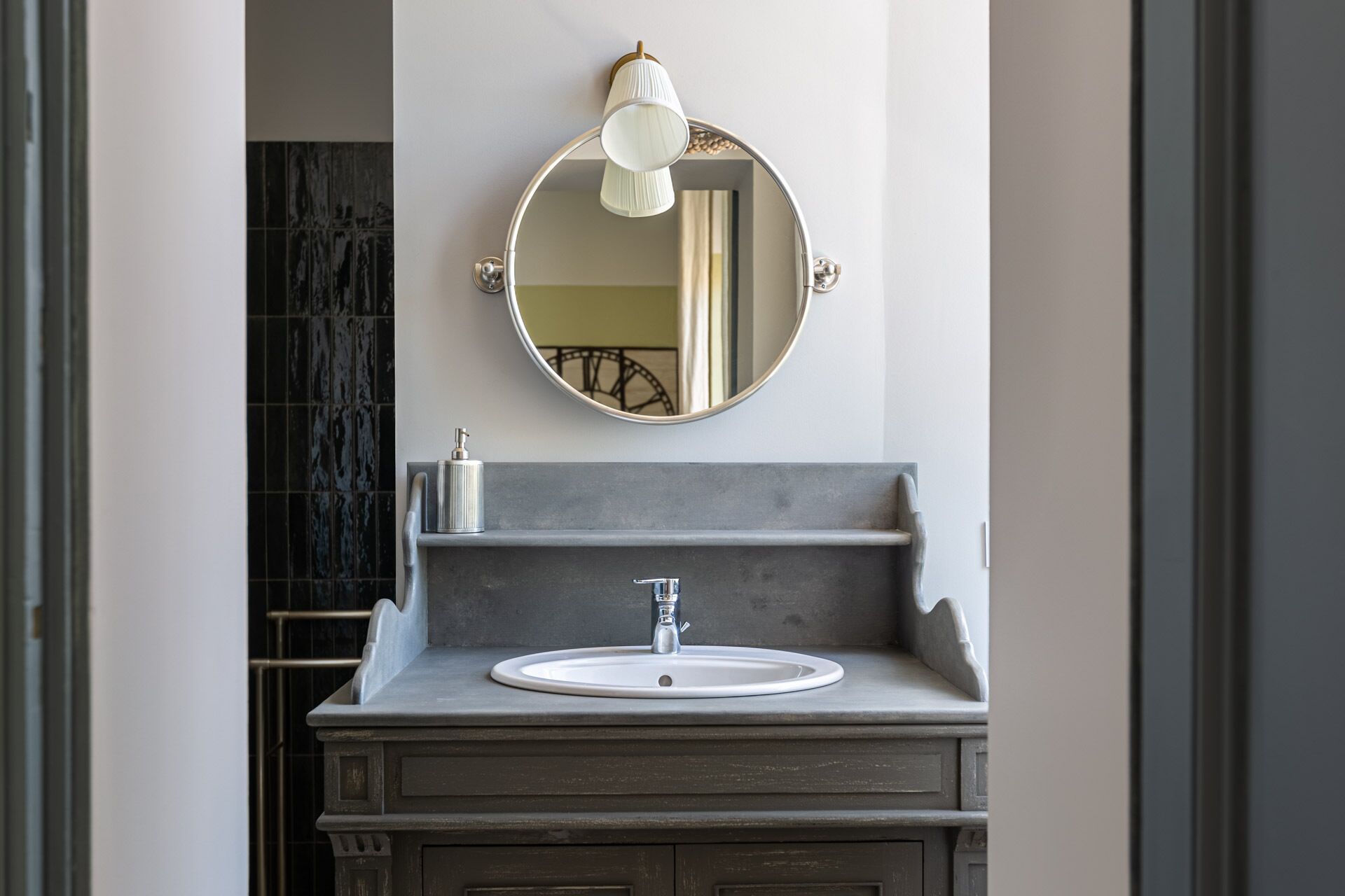 A bathroom with a round mirror, a white sink, and a soap dispenser.