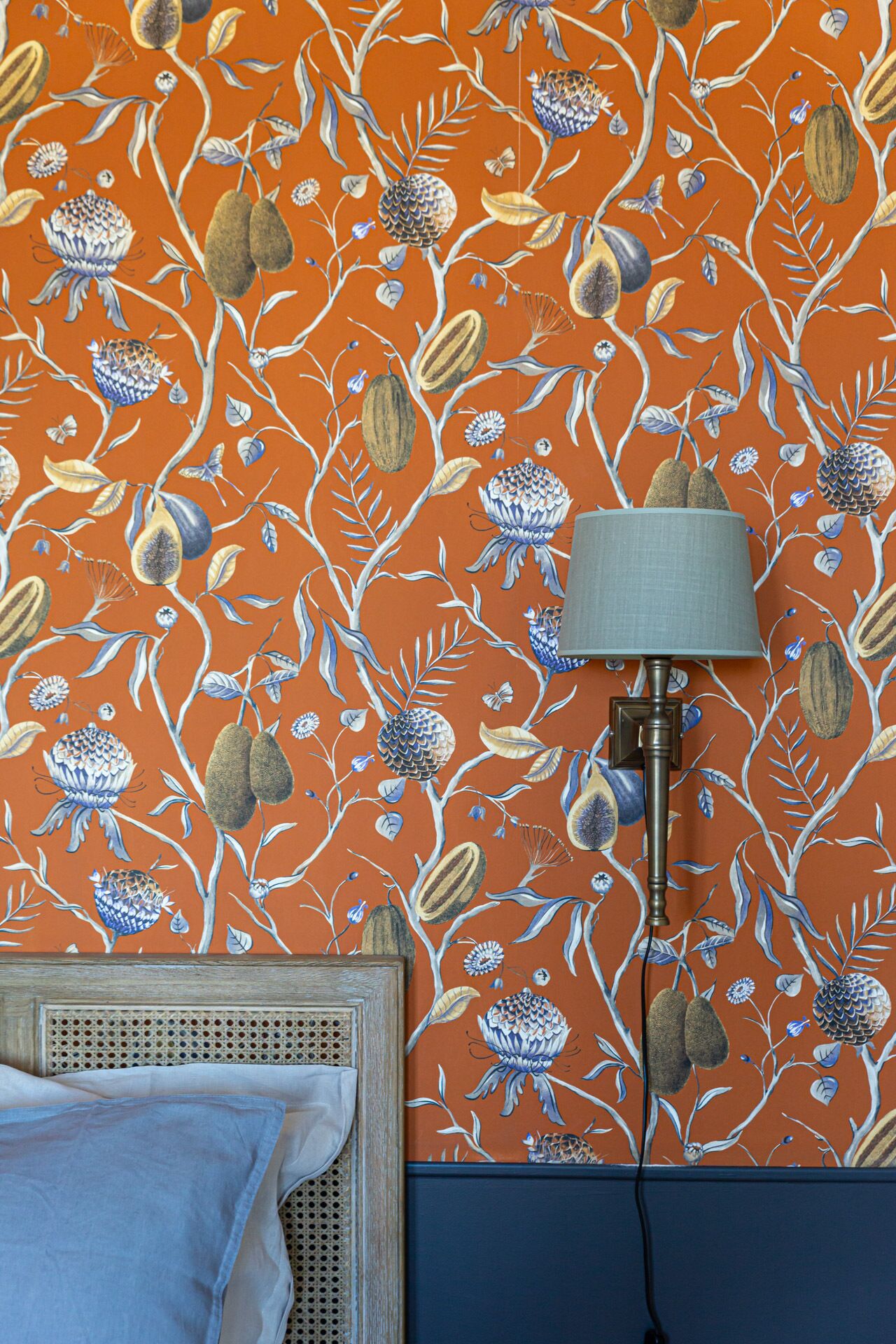 Une pièce avec un papier peint à motifs, une lampe, un lit avec une tête de lit et un mur bleu.