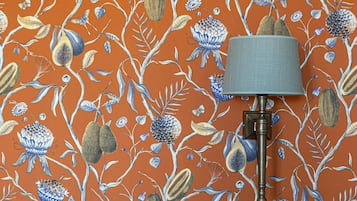 Une pièce avec un papier peint à motifs, une lampe, un lit avec une tête de lit et un mur bleu.