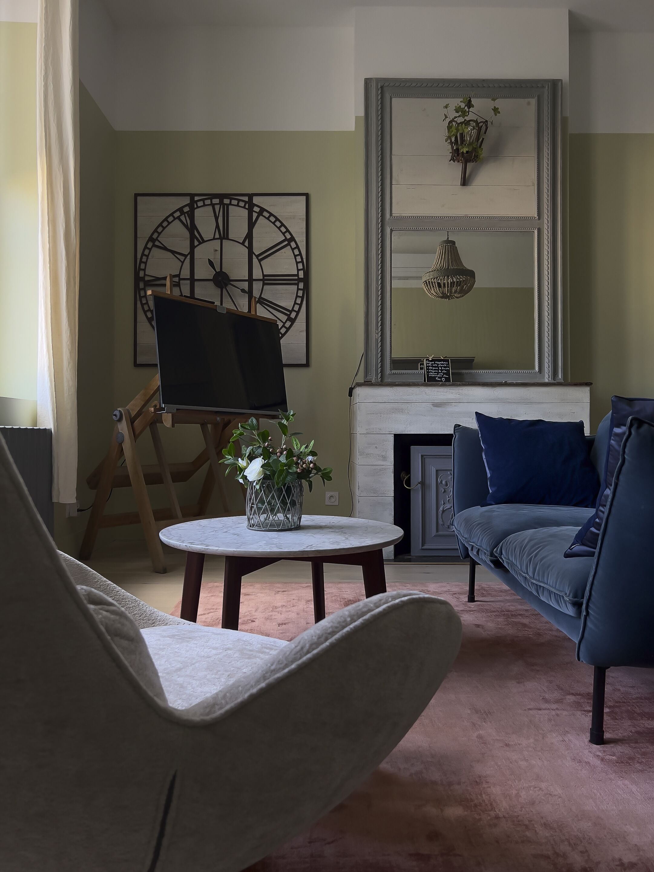 Un salon avec une cheminée, une horloge et un tableau posé sur un chevalet.