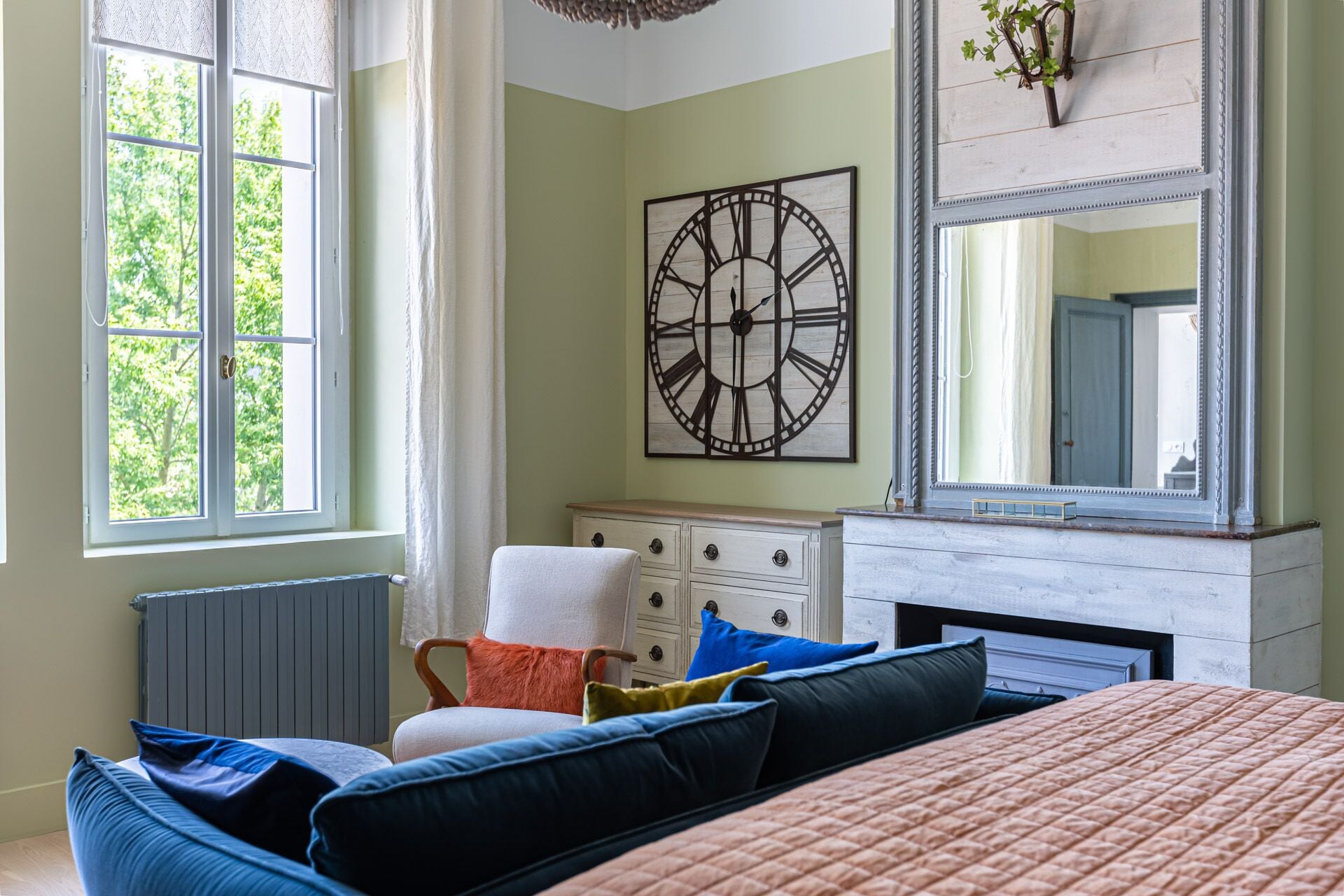 Quarto com uma cama grande, cômoda, espelho e relógio de parede.