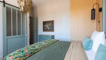 Een slaapkamer met een bed, een linnenkast, een deur, een wandlamp en behang met een bloemmotief.