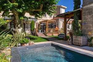 Un área de piscina con una pérgola, mobiliario exterior y un edificio de piedra al fondo.