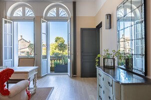 Habitación amplia con un gran ventanal que da a un balcón, un aparador blanco con puertas de cristal y una silla roja.