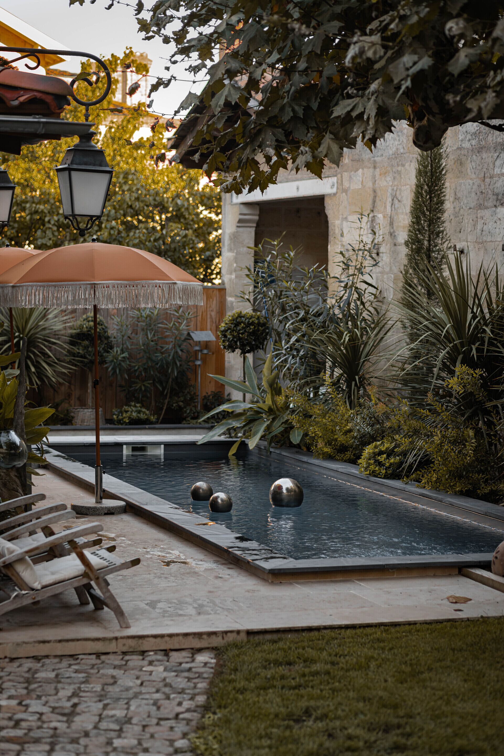 A pool area with a pergola, lounge chairs, and a stone wall.