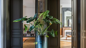 A large potted plant in a metallic vase at the entrance of a room with patterned flooring and a fireplace in the background. - La Maison Mulato Bordeaux, Saint-emilion (Libourne)