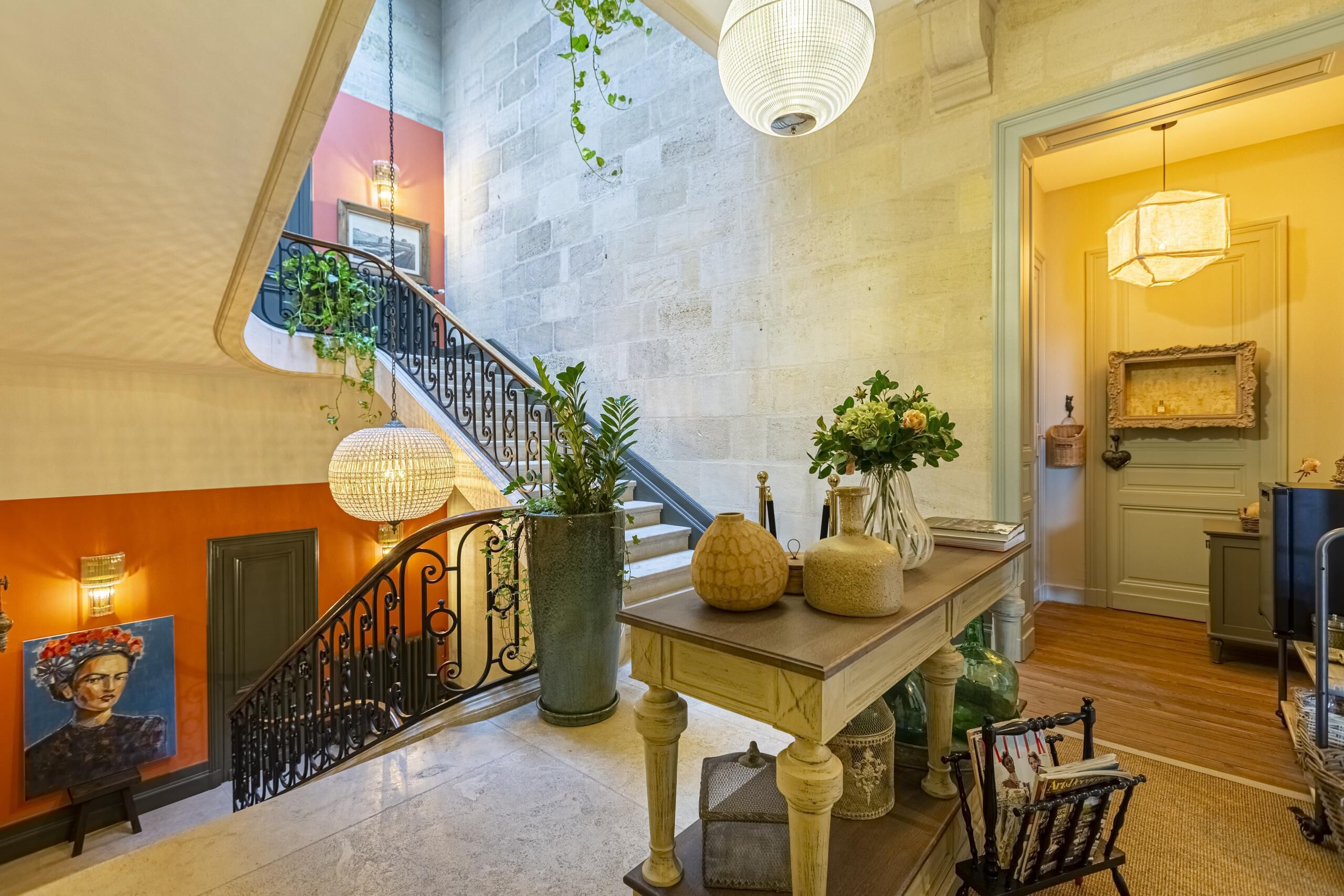 Un magnifique escalier avec une rampe en fer forgé, un grand vase et une table ornée d’objets décoratifs.
